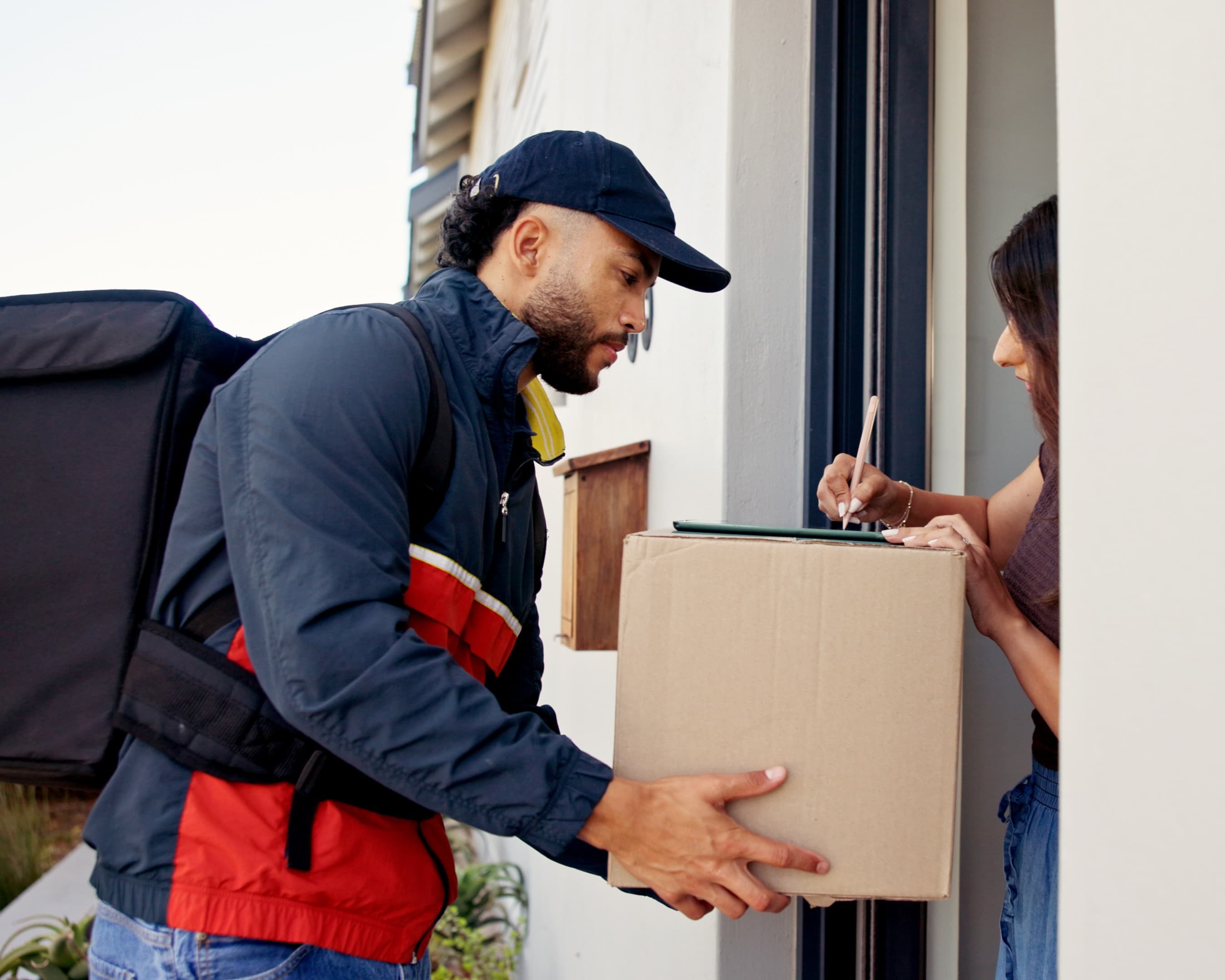 Courier with delivery backpack handing a parcel to a customer for signature at the door